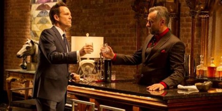 Dean Winters as Avi next to Michael Nyqvist as Viggo Tarasov holding glasses in John Wick 