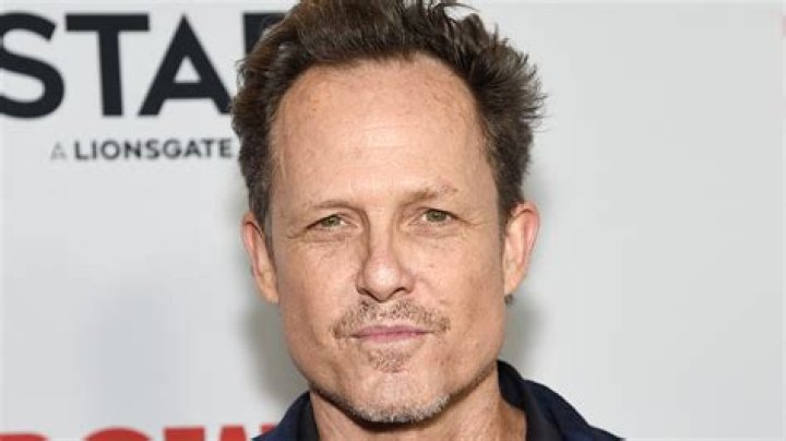 Dean Winters as The Vulture sitting at Amy's desk in Brooklyn Nine-Nine