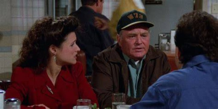 Elaine and Jerry sitting at a table with an older man in a hat in Seinfeld